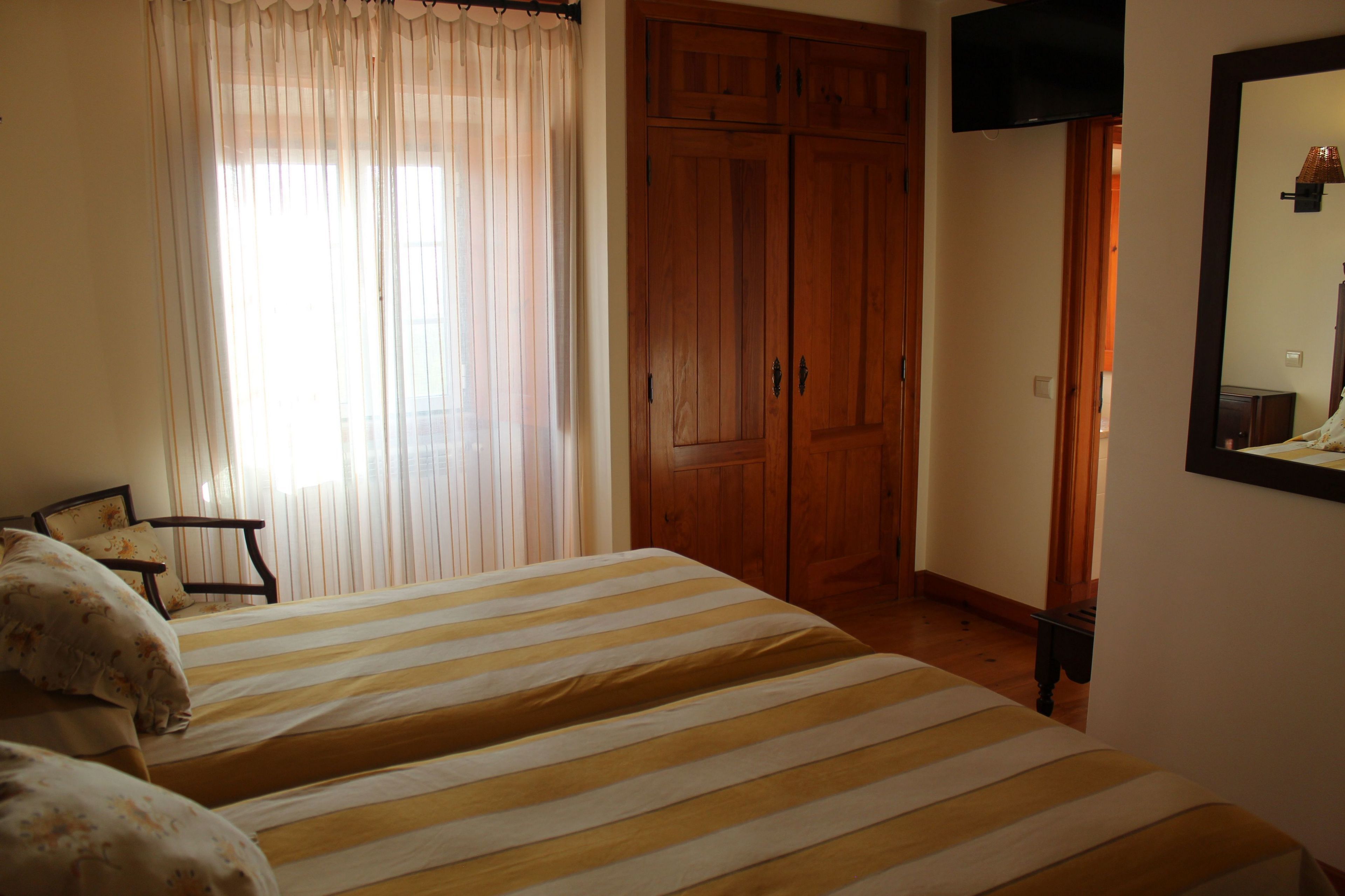 Een slaapkamer met twee bedden, een houten garderobe, een televisie en een spiegel aan de muur.