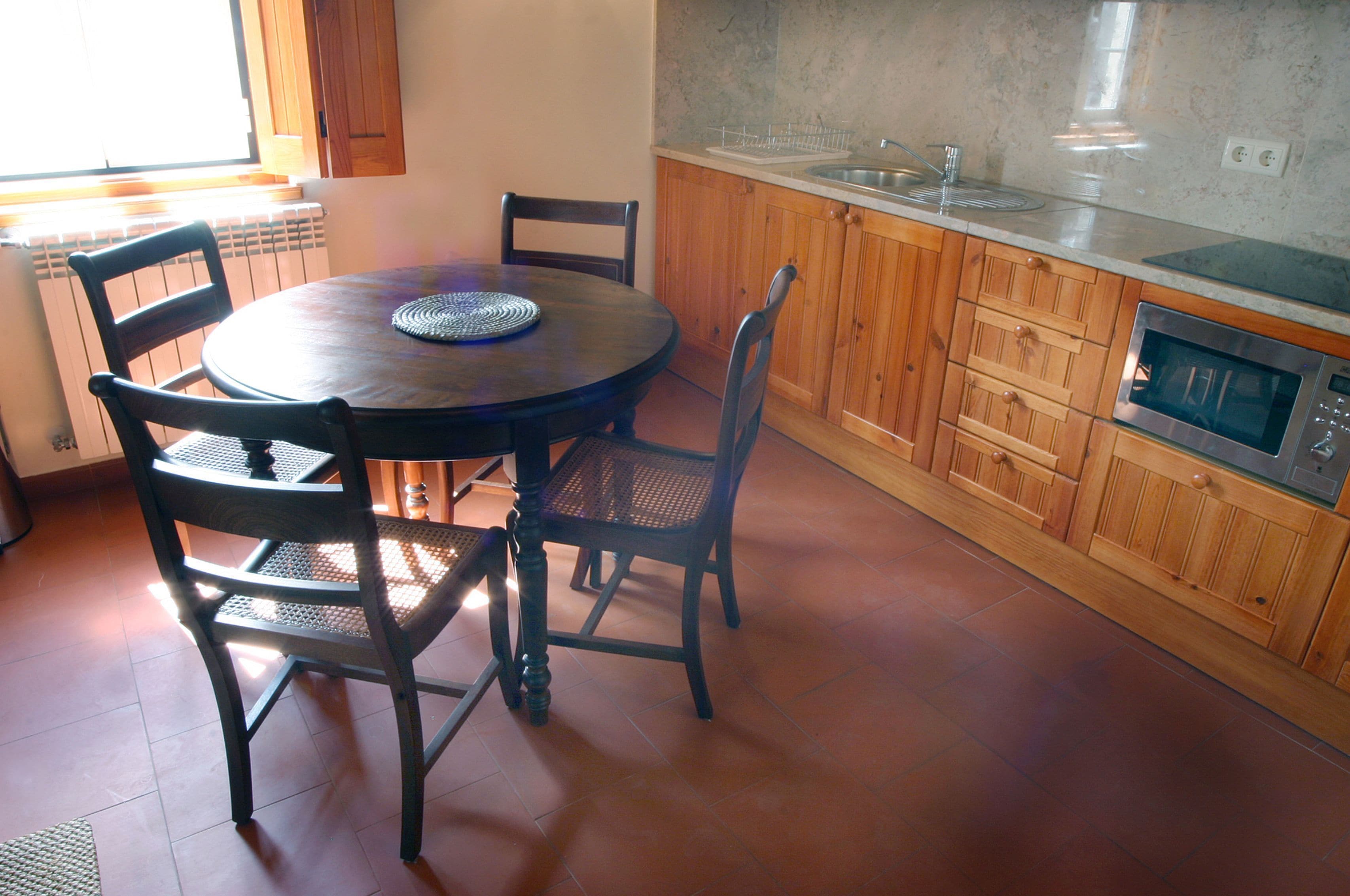 A kitchen with a round table, four chairs, wooden cabinets, a built-in oven, and a window providing natural light.