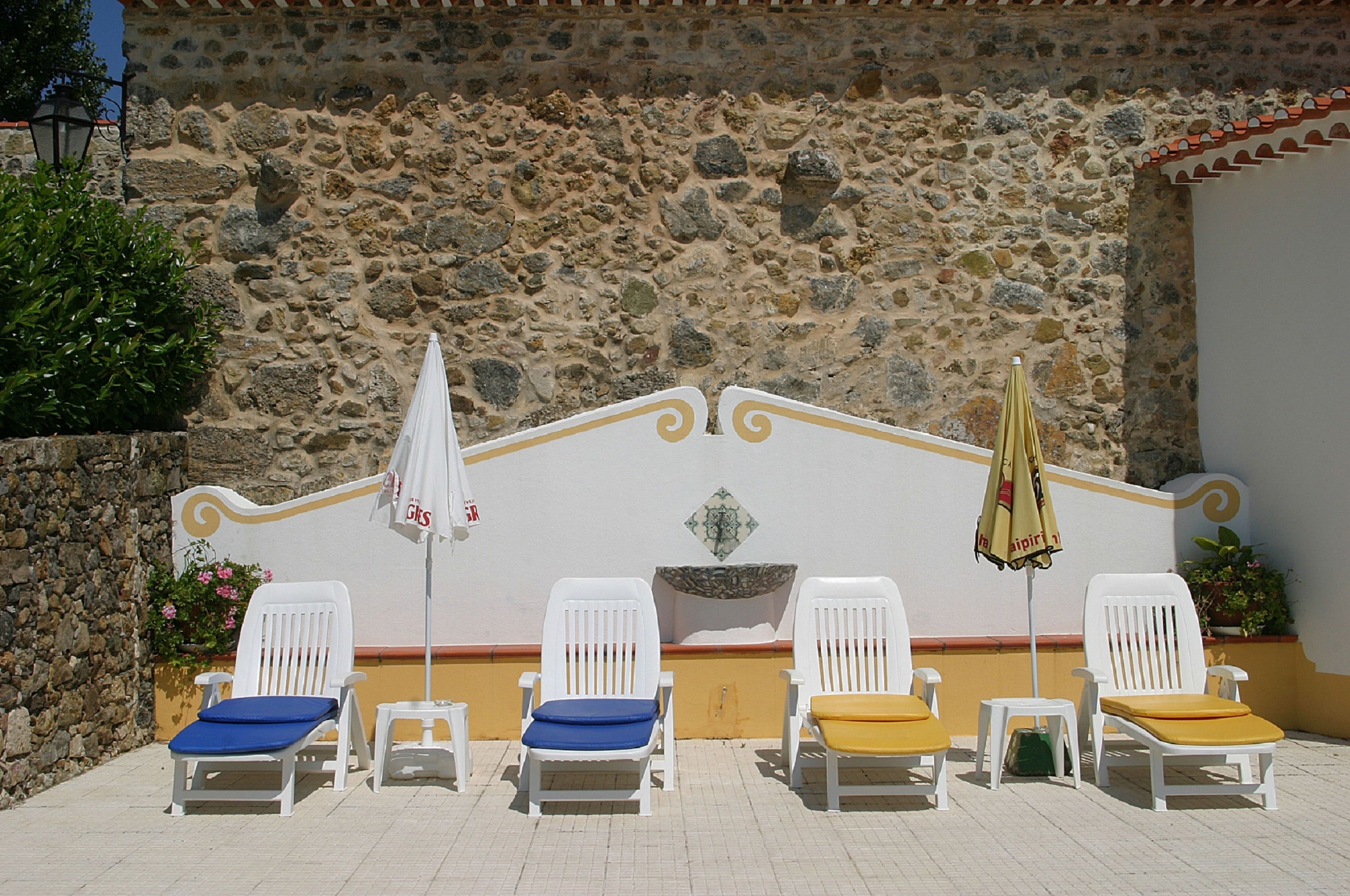 Filea di poltrone bianche con cuscini blu e gialli, disposte di fronte a un muro in pietra con uno stemma decorativo.