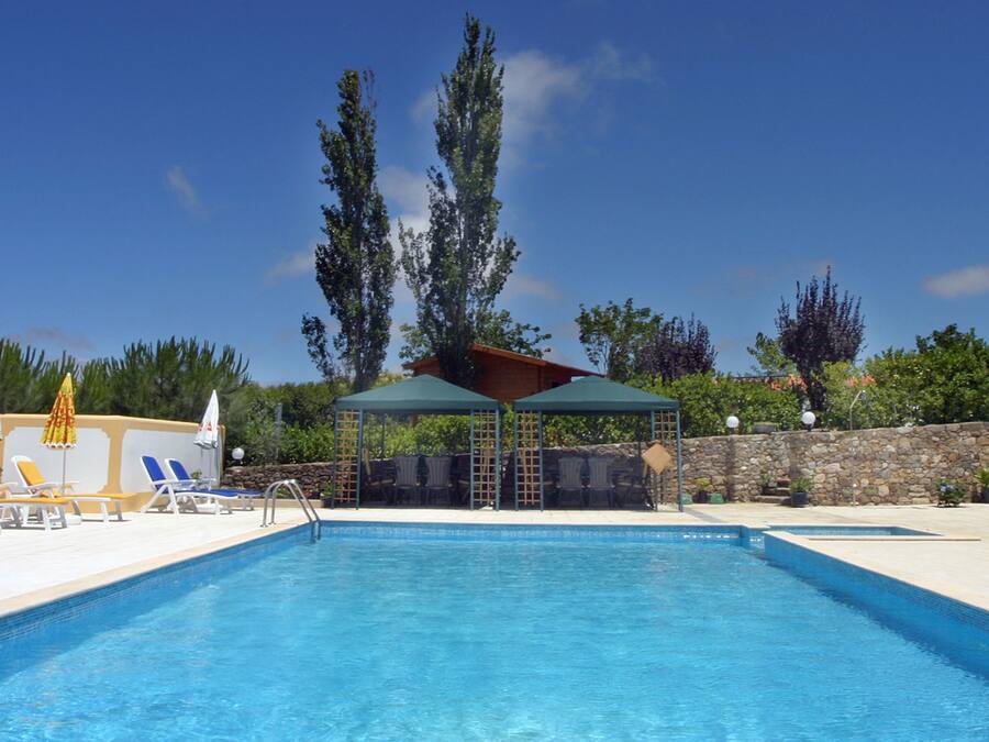 A swimming pool with lounge chairs and umbrellas, surrounded by a stone wall and trees.