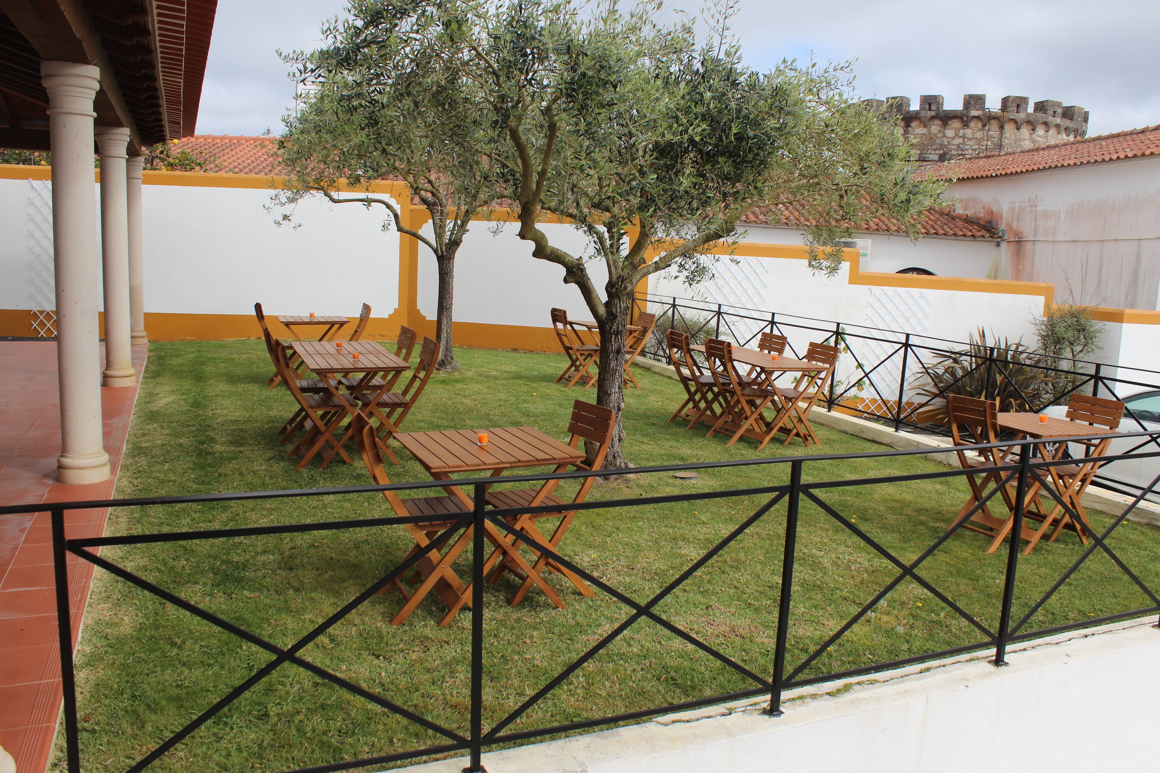 An outdoor seating area with tables and chairs, surrounded by a low fence, and a tree in the center.