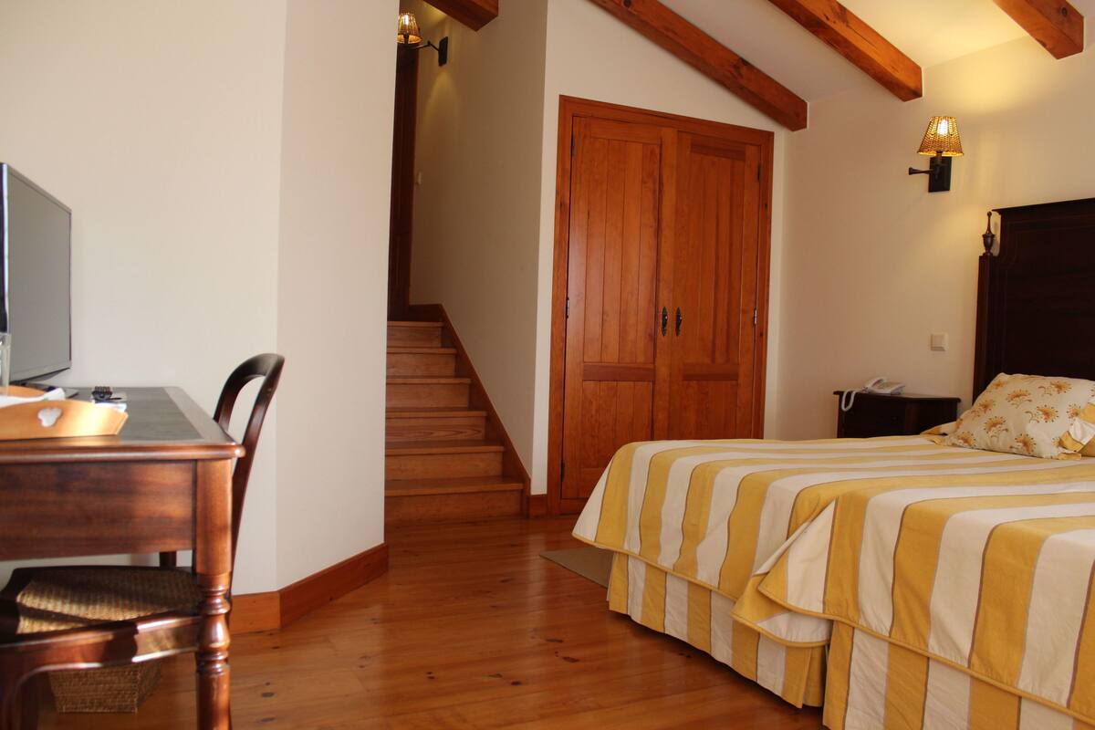 A bedroom with two beds, a wooden desk, a chair, a staircase, and a wooden door.