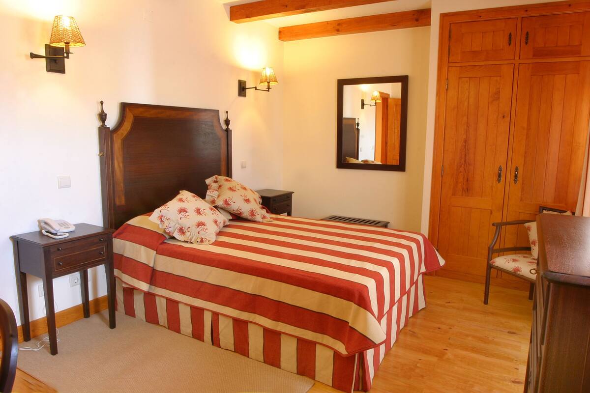 A bedroom with a wooden bed, bedside lamps, a mirror, and a wardrobe.
