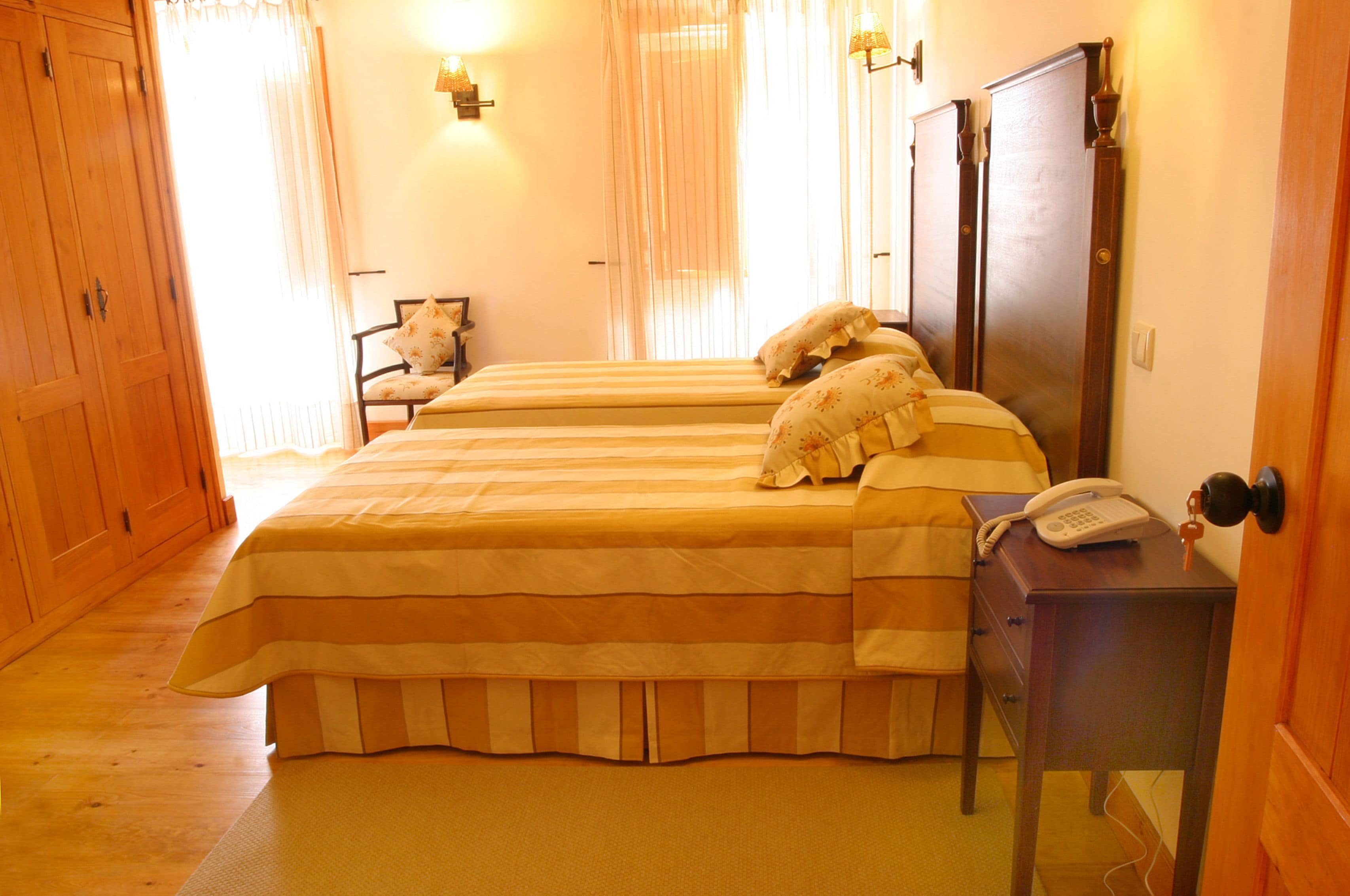 A room with two beds, a wooden wardrobe, a bedside table with a phone, and a chair.