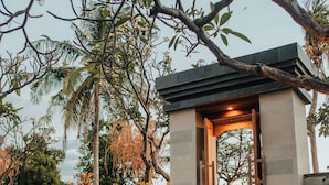 A garden entrance with a stone pathway leading to a wooden door, surrounded by lush greenery and palm trees. - New Sunari Lovina Beach Resort (Buleleng)
