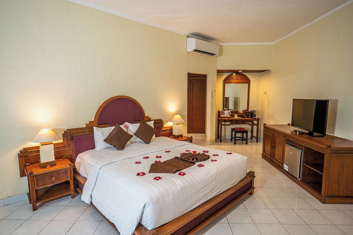Une chambre d’hôtel avec un grand lit, deux tables de chevet avec des lampes, une télévision, un petit réfrigérateur et un miroir au-dessus de la commode.