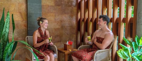 Two people seated at a table with drinks, in a room with stone walls and wooden furniture.
