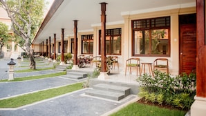 A hotel with a covered outdoor seating area, steps leading to the entrance, and a garden with plants and a tree. - New Sunari Lovina Beach Resort (Buleleng)