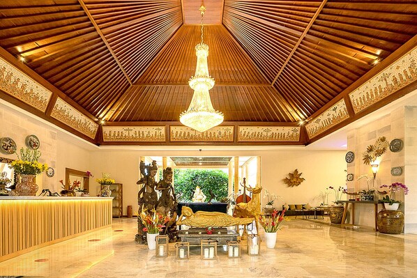 Un vestíbulo espacioso con un alto techo de madera, un candelabro central y un mostrador de recepción.