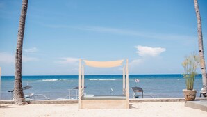 A beach with a wooden canopy, palm trees, and a view of the ocean. - New Sunari Lovina Beach Resort (Buleleng)