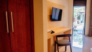 Una habitación con un armario de madera, un televisor montado en la pared, un escritorio de madera y una silla.