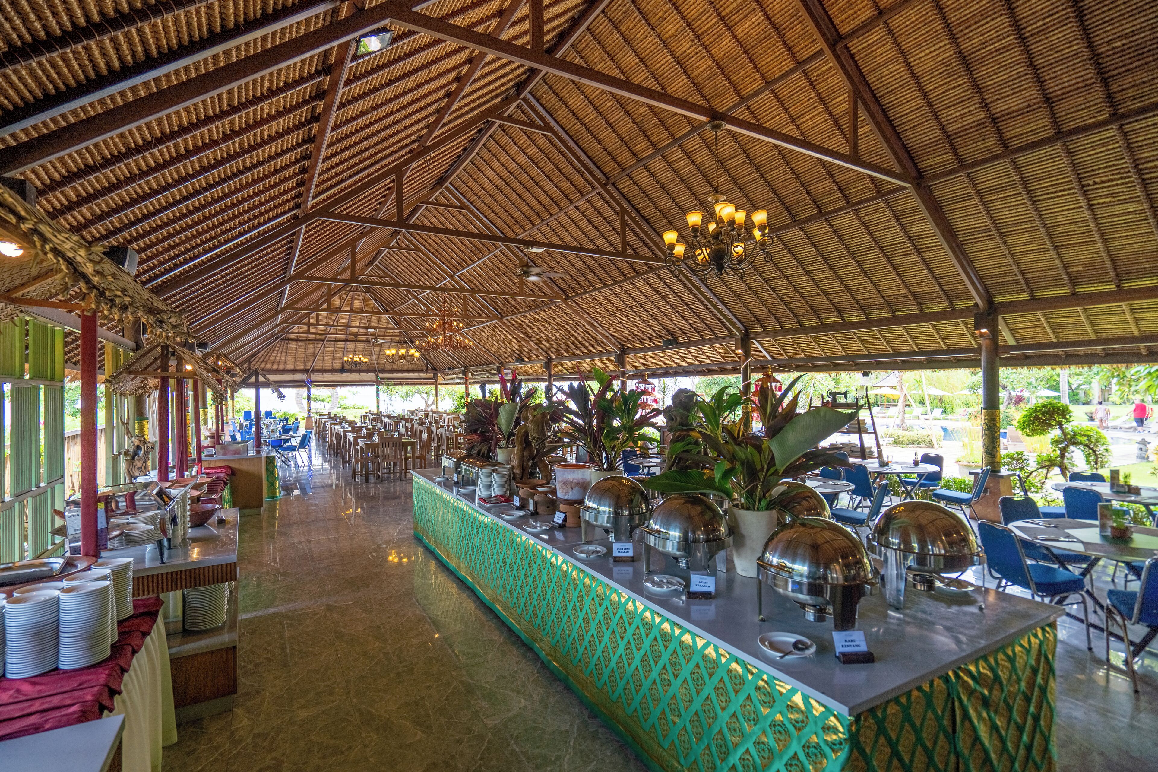 A spacious indoor area with a high ceiling, a buffet counter with food service equipment, and outdoor seating with tables and chairs.
