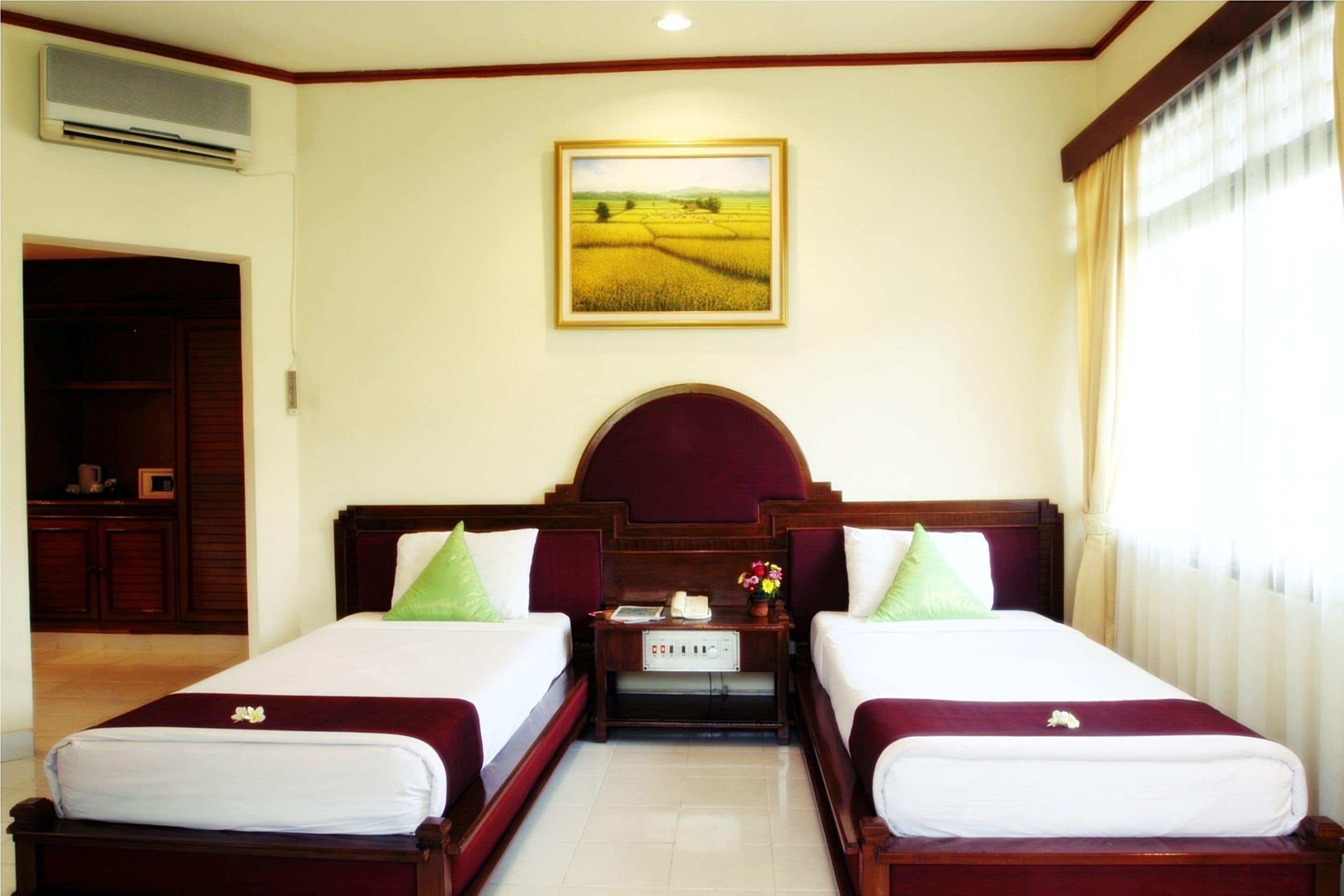 A hotel room with two beds, a nightstand, a painting of a field, and a wardrobe.