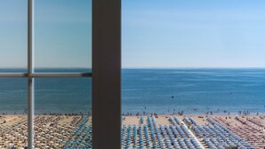 Ein Strand mit Reihen von Sonnenschirmen und Liegestühlen, freier Blick auf den Ozean und ein Gebäude im Vordergrund.