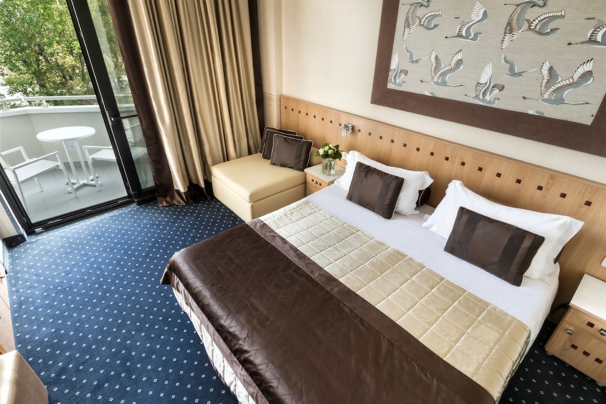 Ein Hotelzimmer mit einem großen Bett, einem kleinen Sofa, einem Nachttisch und Blick ins Freie.