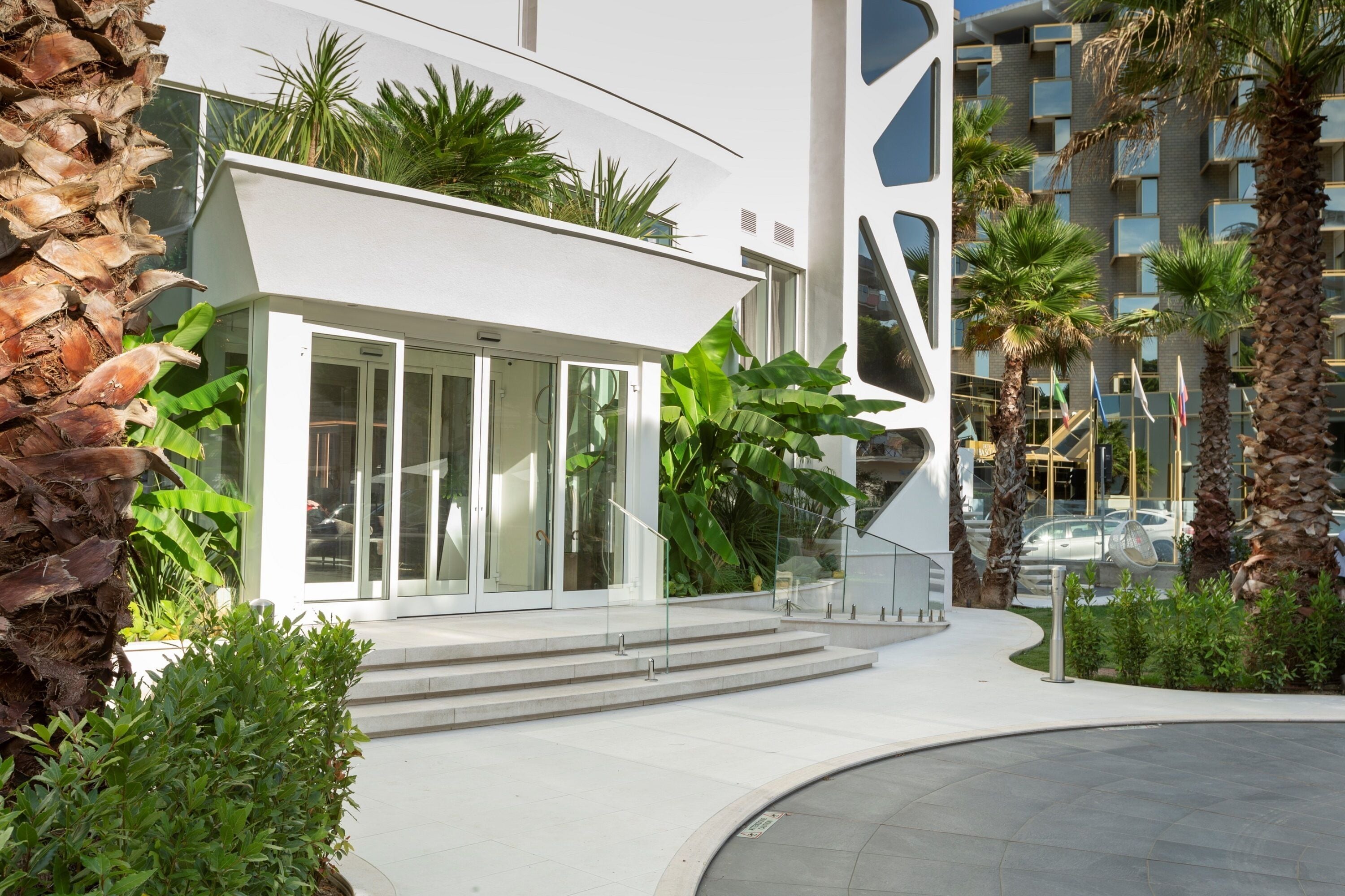 Un bâtiment moderne avec une entrée en verre, entouré de palmiers et de verdure.