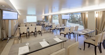 Un salón de conferencias con varias mesas y sillas, equipado con pantallas y material de presentación.