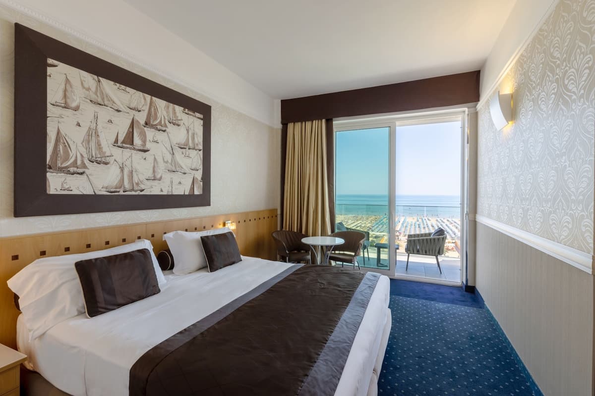 Ein Hotelzimmer mit einem großen Bett, Meerblick, einem kleinen Tisch und einem Stuhl.