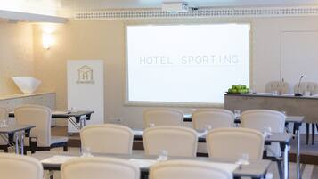 Et mødelokale med et projektionslærred, der viser "HOTEL SPORTING LUXURY LIVING".