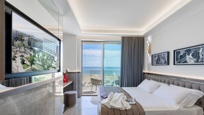 Ein modernes Hotelzimmer mit einem großen Bett, einer Sitzecke, einem Fernseher und einem Balkon mit Blick auf die Stadt.