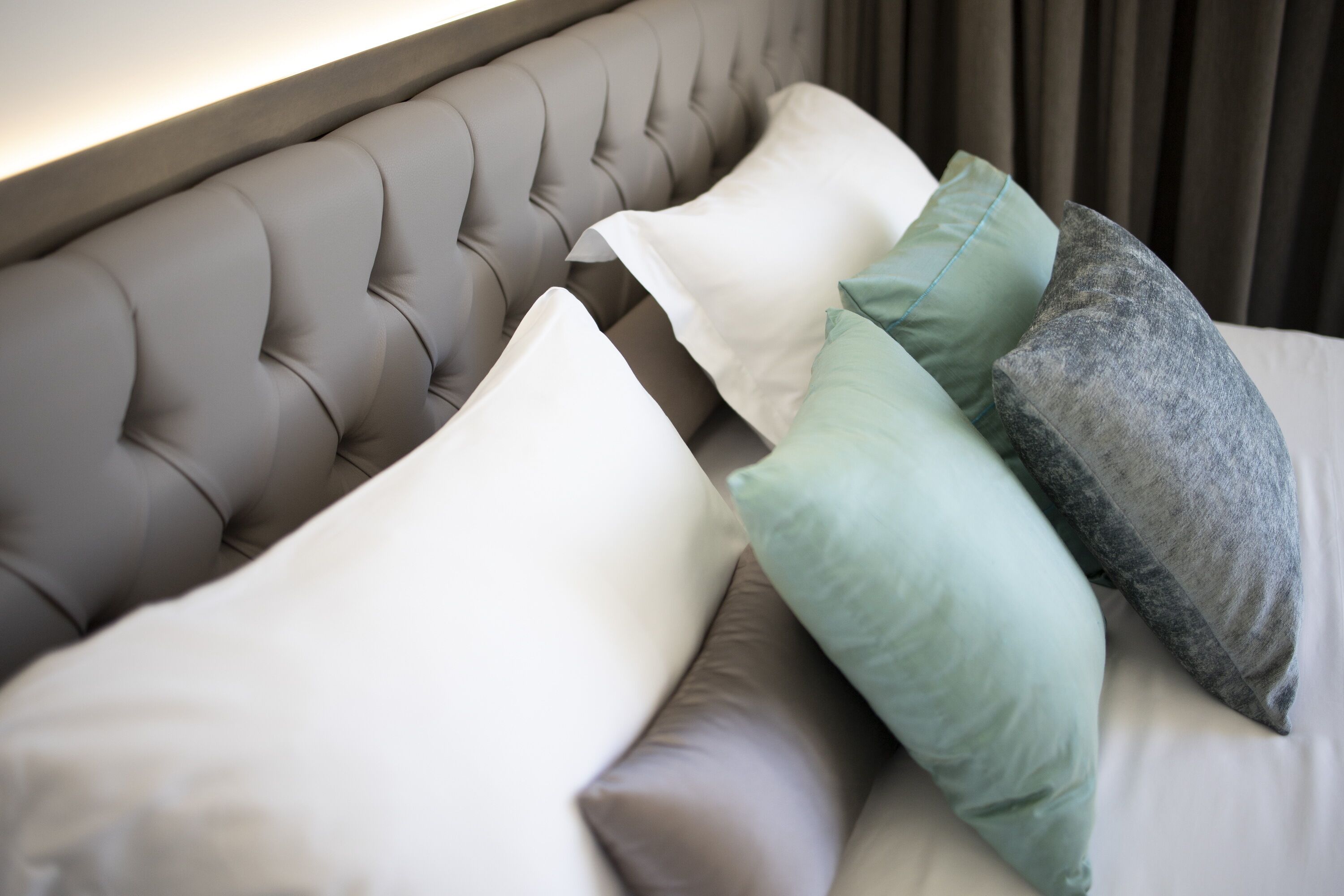 Un lit doté d’une tête de lit capitonnée et de plusieurs coussins de différentes couleurs.