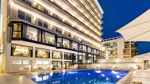 Ein modernes Hotel mit großem Innenpool, mehreren Balkonen und gut beleuchteten Außenbereichen.