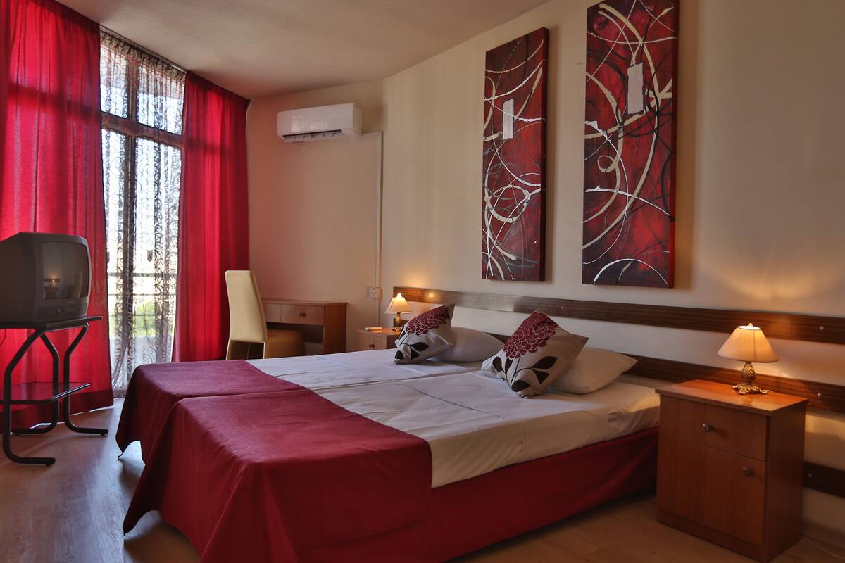 A hotel room with a large bed, a desk, a chair, and a TV.