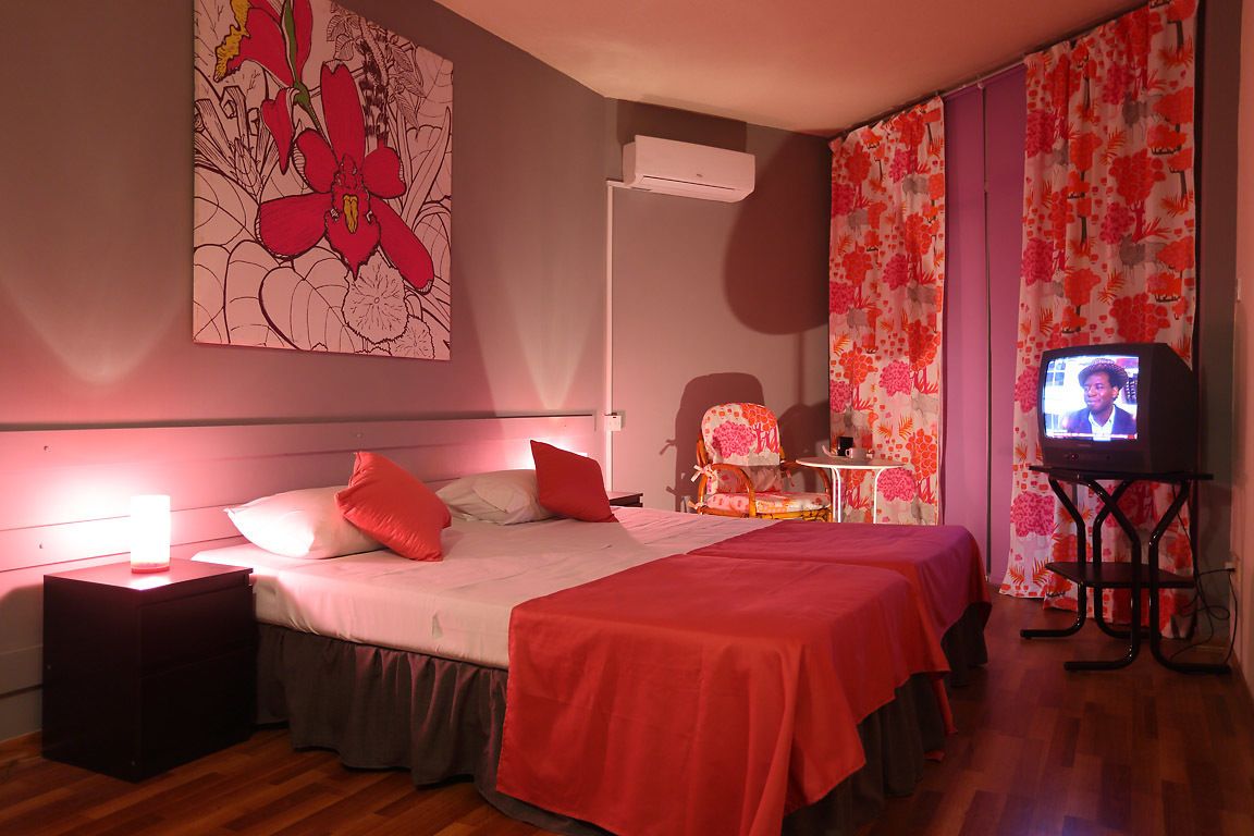A bedroom with two beds, a TV, a nightstand, and a wall-mounted air conditioner.