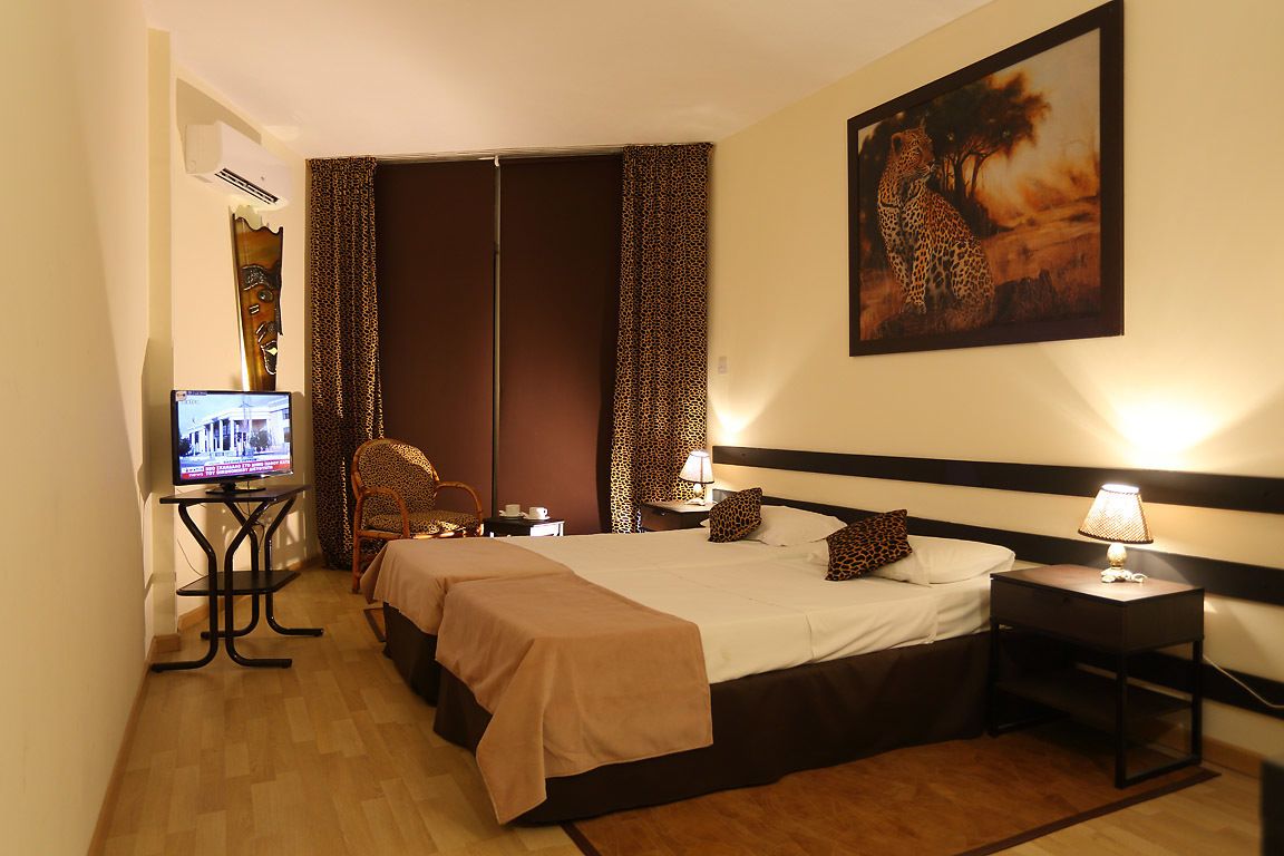 A hotel room with a bed, a desk with a computer, a chair, and a leopard print curtain.
