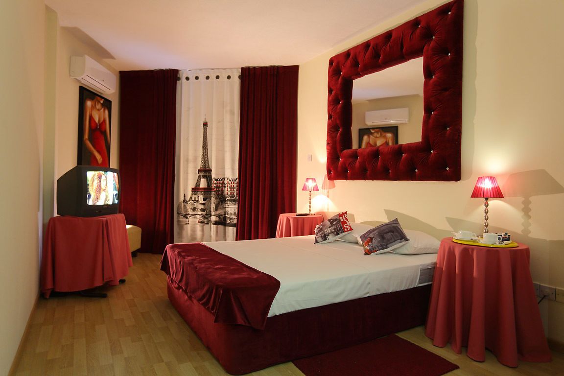 A hotel room with a bed, a television, a mirror, and a red curtain.