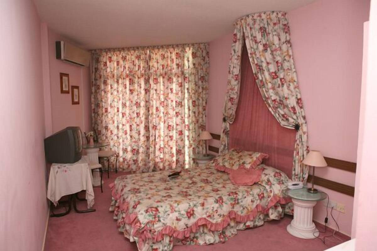 A bedroom with a floral bedspread, a canopy bed, a television, a bedside table, and a lamp.