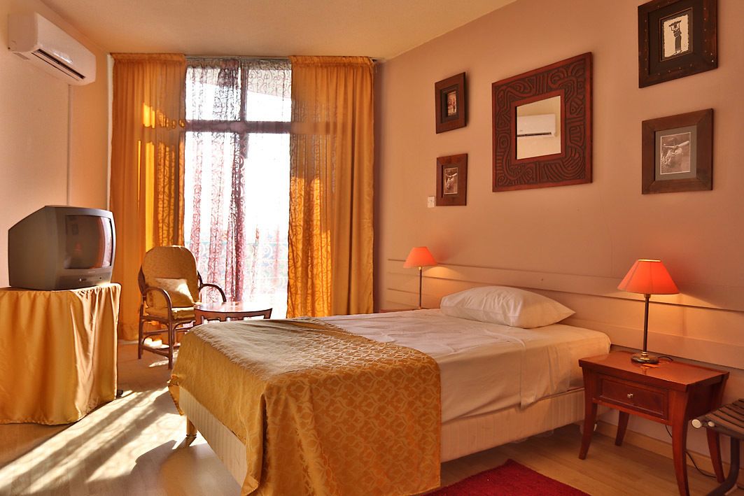 Una camera d'albergo con un letto, lampade da comodino, televisione, una sedia e una finestra con tende.