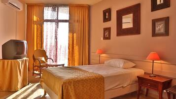 Una camera d'albergo con un letto, lampade da comodino, televisione, una sedia e una finestra con tende.