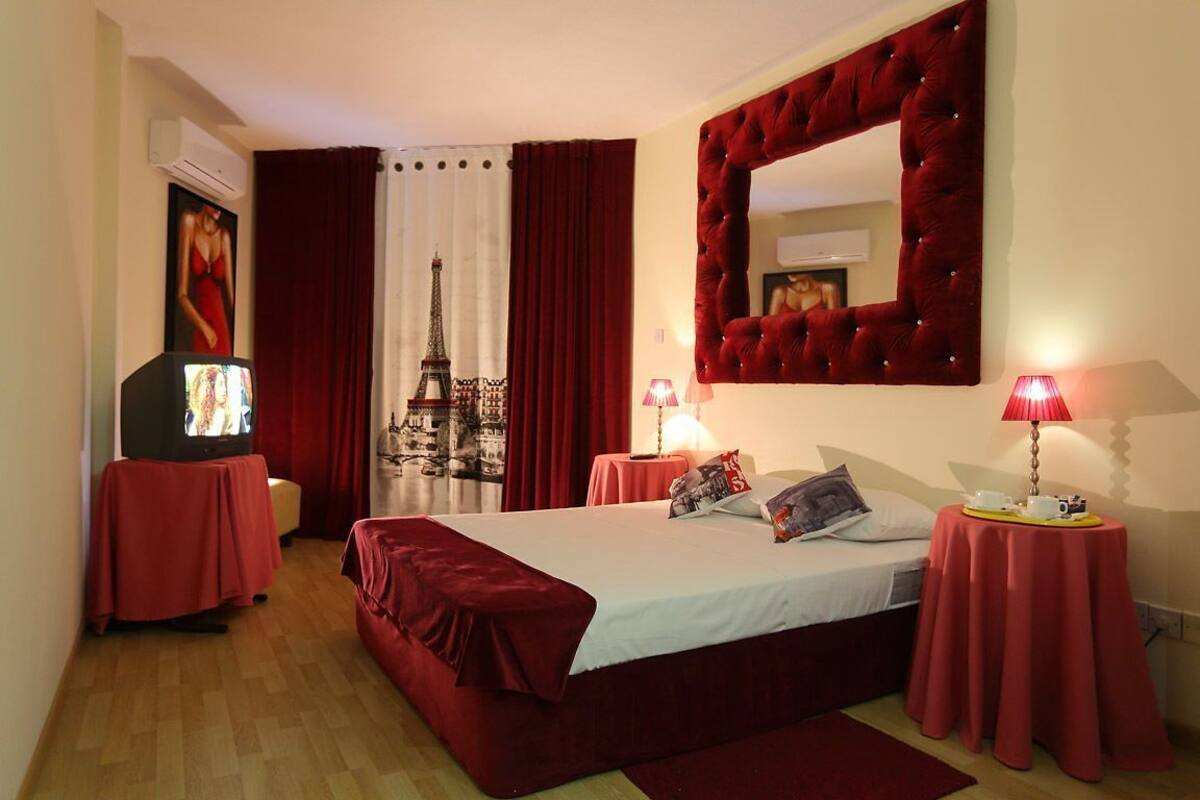 A hotel room with a bed, a television, a red curtain, a mirror, and a lamp.