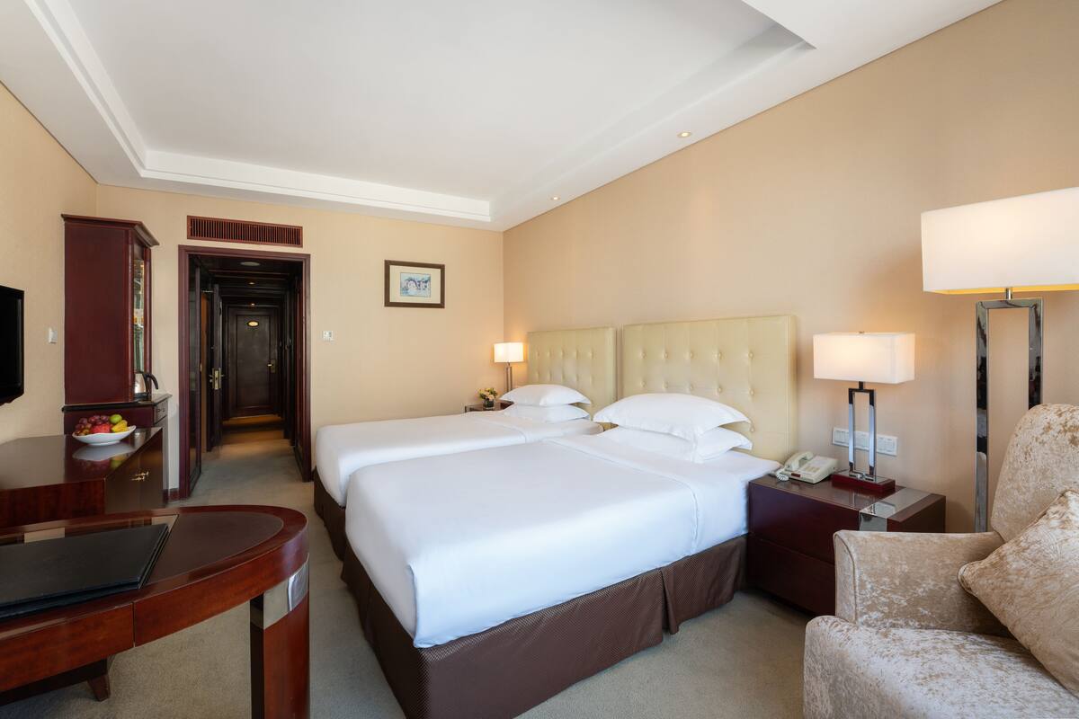 Habitación de hotel con dos camas, un escritorio, una silla, una lámpara y un televisor.