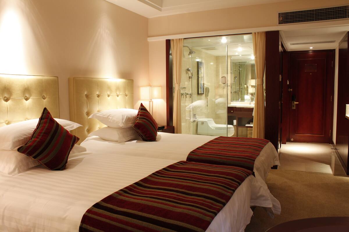 Habitación de hotel con dos camas, baño y cabina de ducha de vidrio.