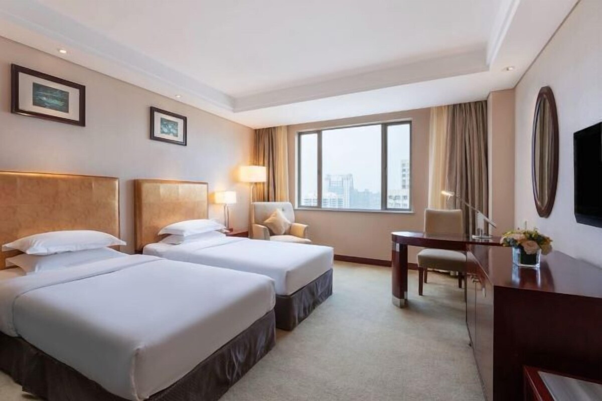 Une chambre d’hôtel avec deux lits, un bureau, une chaise, une télévision et une fenêtre donnant sur la ville.