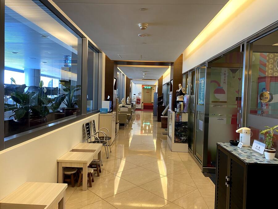 A corridor with a wooden table and chairs, a glass display case, and a mannequin in a store.
