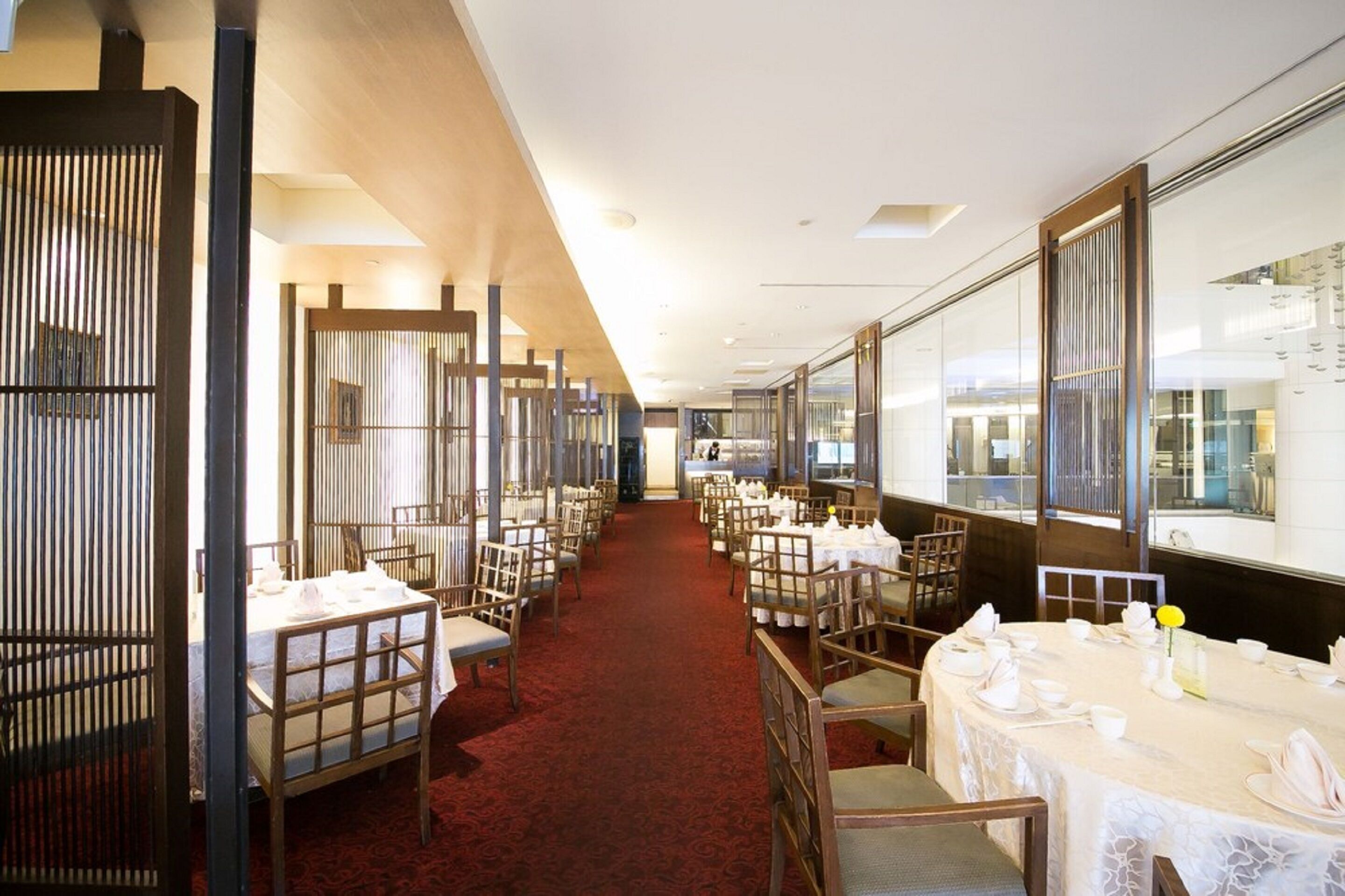 Une salle à manger d’hôtel avec des tables dressées pour le service, un tapis rouge et une vue à travers le mur de verre.