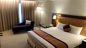 A hotel room with a large bed, a sofa, a nightstand with a lamp, and a window with curtains.
