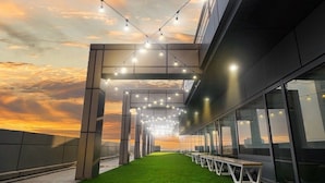 Una terraza al aire libre con césped artificial, luces colgantes y vistas al atardecer.