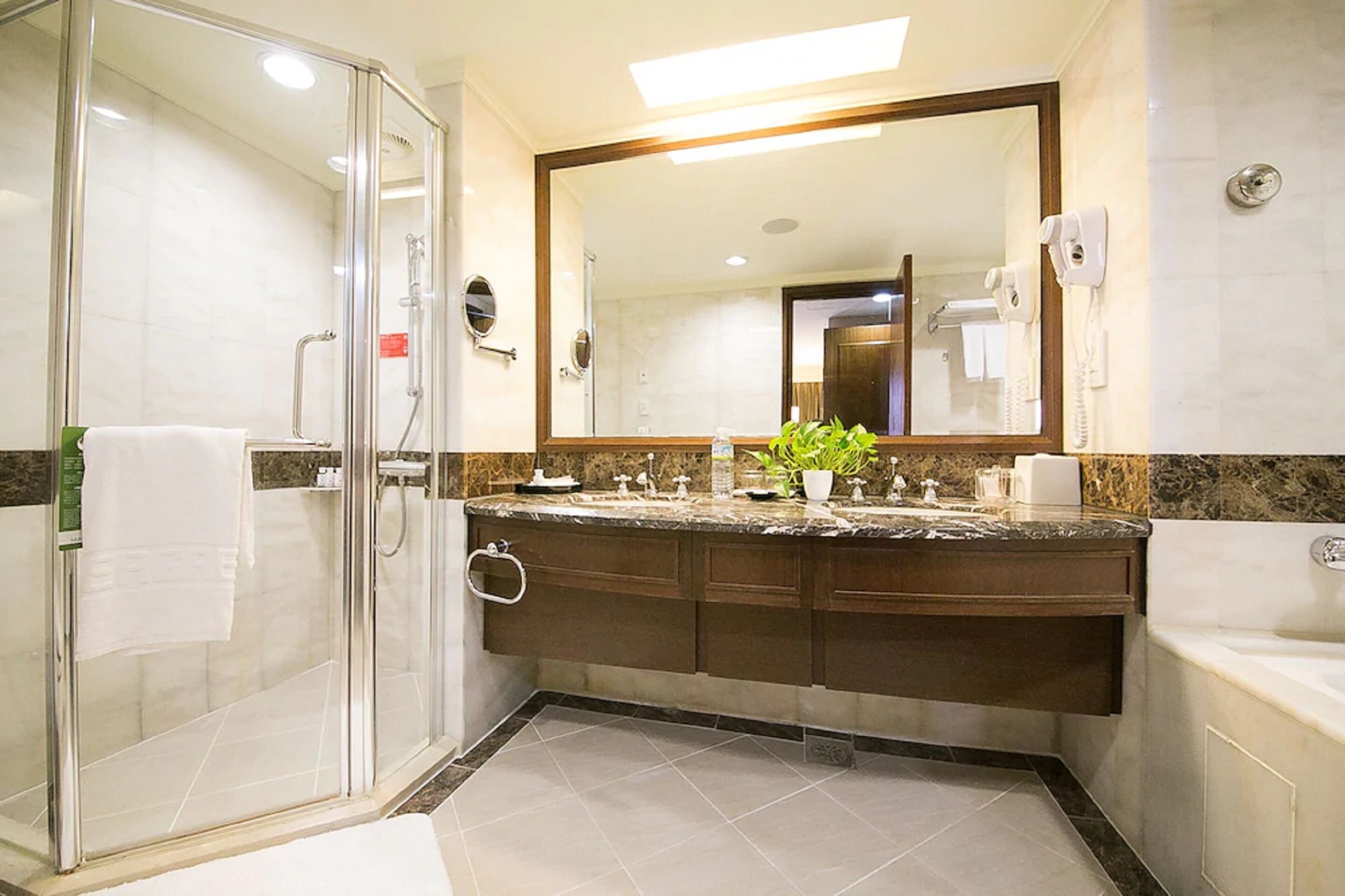 Un baño moderno con ducha envuelta en vidrio, un espejo grande, encimera de mármol y lavamanos integrado.