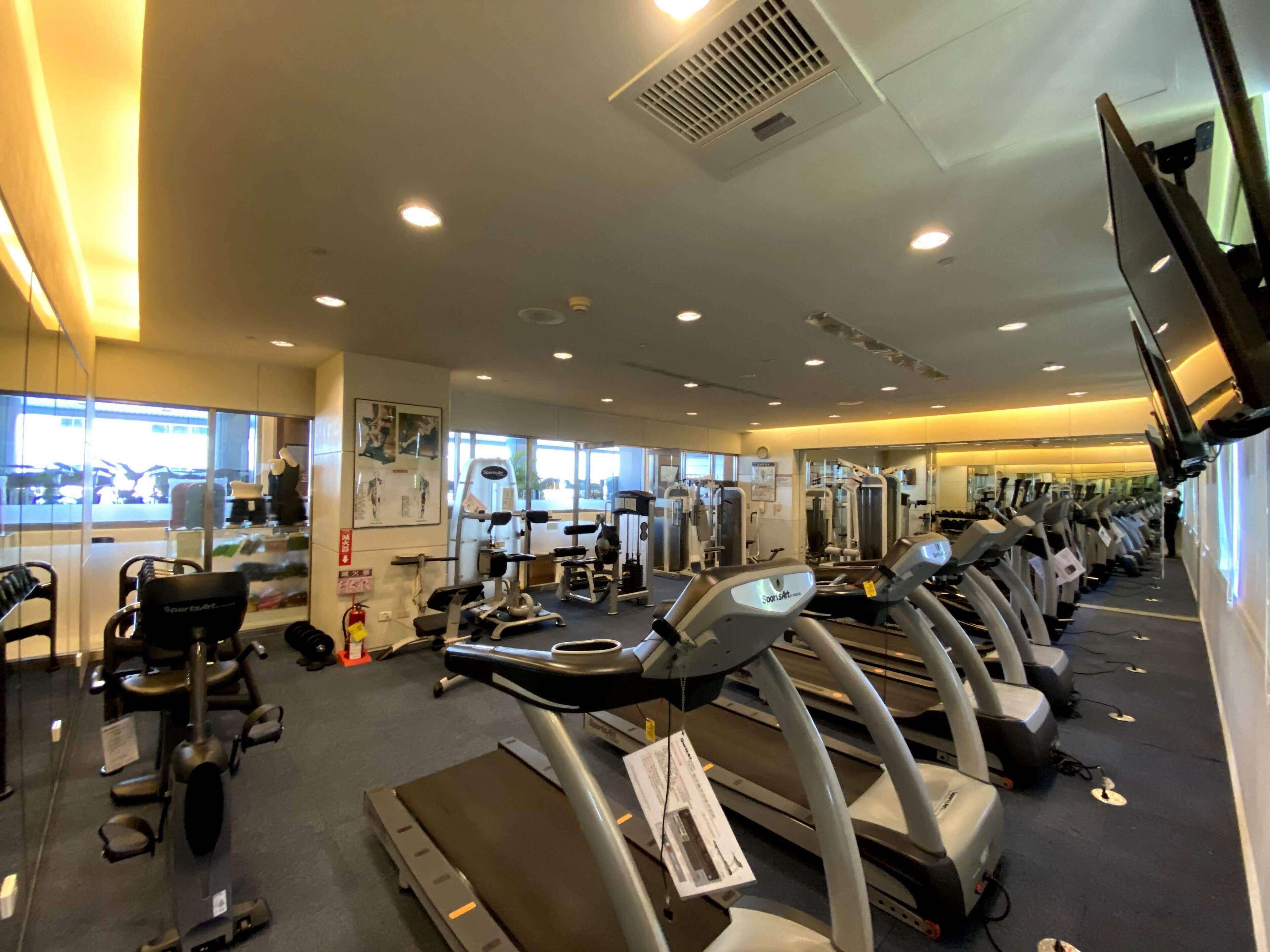 Ein Fitnessstudio mit mehreren Laufbändern, Kraftgeräten und einer Spiegelwand.