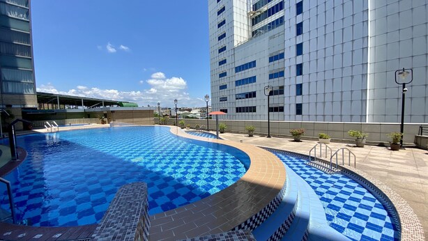 Una piscina con baldosas de diseño ajedrezado, rodeada por un solárium alicatado y un edificio con fachada moderna.