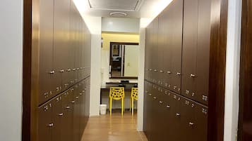 A hallway with wooden lockers, a small kitchenette, and a yellow chair.