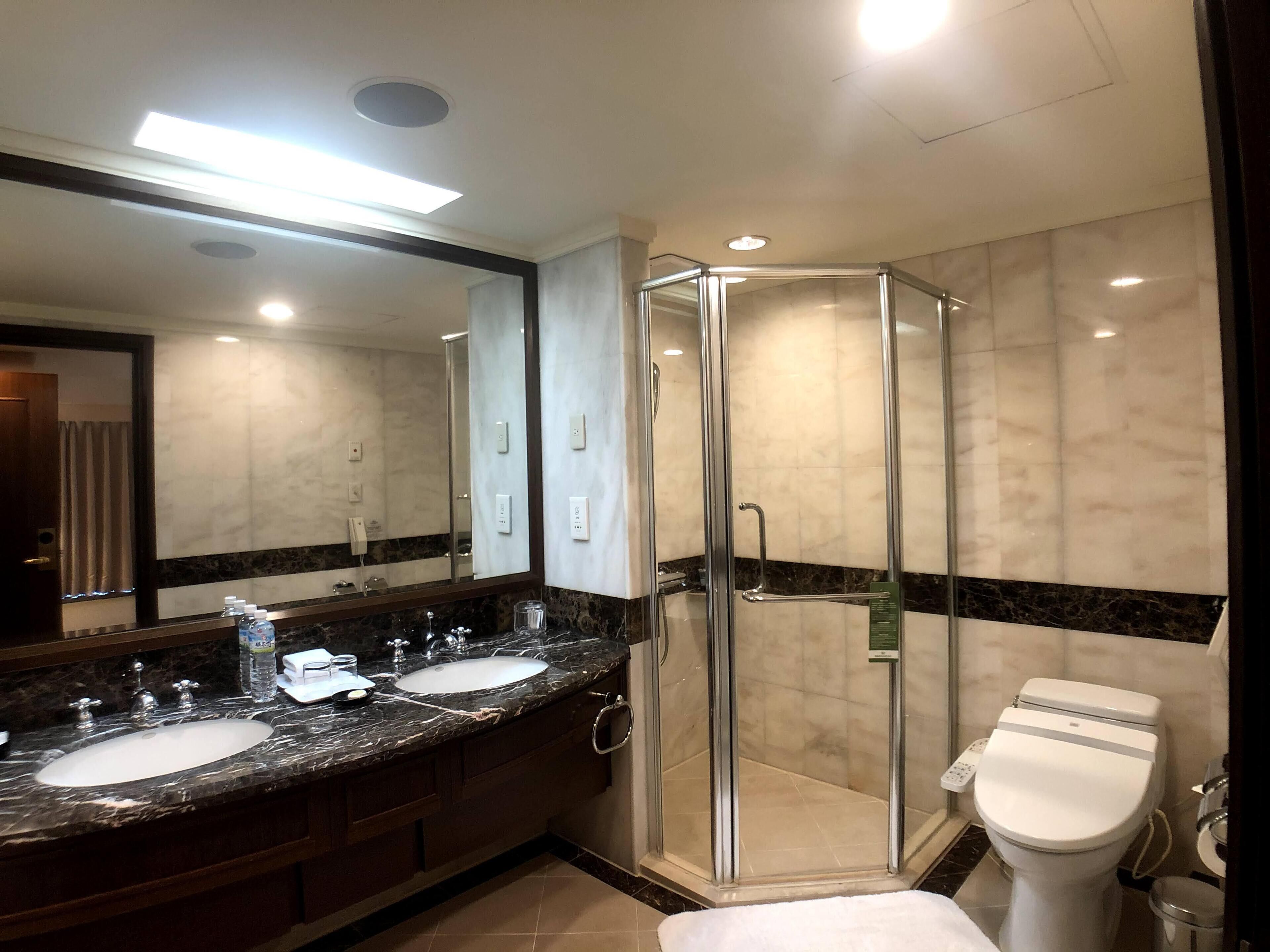 A modern bathroom with a large mirror, two sinks, a shower enclosure, and a toilet.