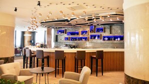 Zona de bar moderna con una barra curva, taburetes y un área de estar con sillas y una mesa pequeña.
