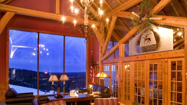 A cozy interior with a large window overlooking a snowy landscape, wooden furniture, and a sign for 'PONTRESINA RESTORANTE'. - Otsego Resort (Gaylord)