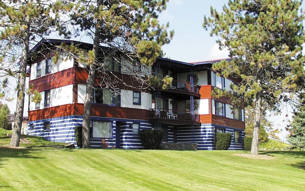A multi-story building with a distinctive striped facade, a balcony on the second floor, and a well-maintained lawn in front.