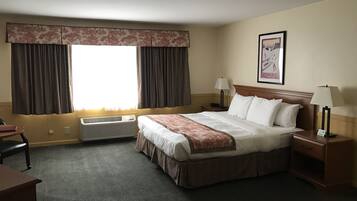 Ett hotellrum med en säng, två sängbord med lampor, ett skrivbord, en luftkonditionering och ett fönster med gardiner.